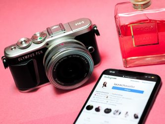 A camera and bottle of perfume next to a smartphone.