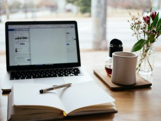 A notepad, pen and mug next to a laptop.